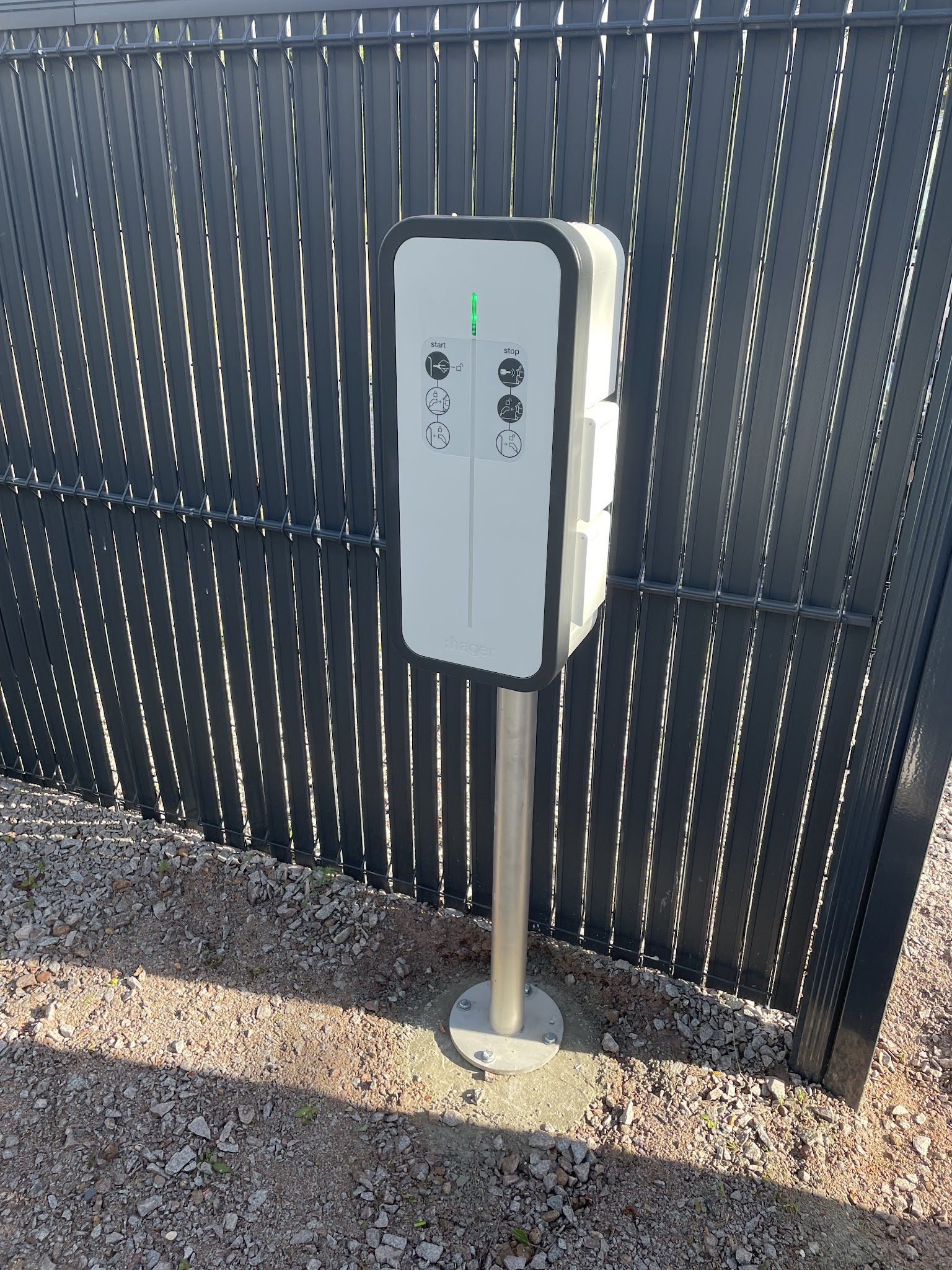 Borne de recharge sur pied devant une clôture anthracite